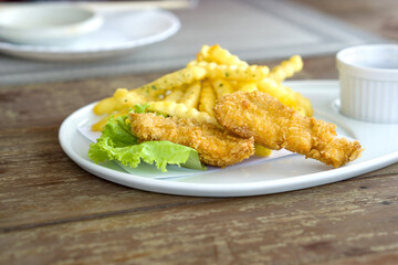 A plate with crispy fish served with golden potato fries on a wooden table.