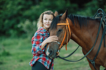 Happy blonde with horse in forest. Woman and a horse walking through the field during the day....
