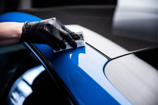 Car cash or car detailing studio worker applying graphene or ceramic coating on blue sport car.