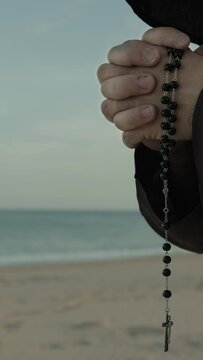 Religious Hands Of A Monk Praying Rosary On The Beach