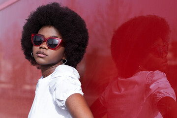 Fashionable young Afro woman wearing sunglasses in front of red window