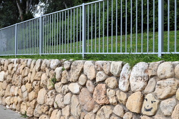 Green plants and flowers grow along a fence in a city park.