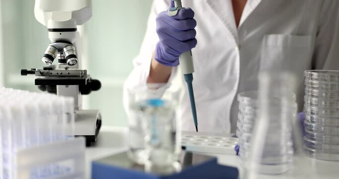 Chemist drips reagent with pipette while clear solution mixes in glass on shaker. Woman does research of liquid substance in laboratory