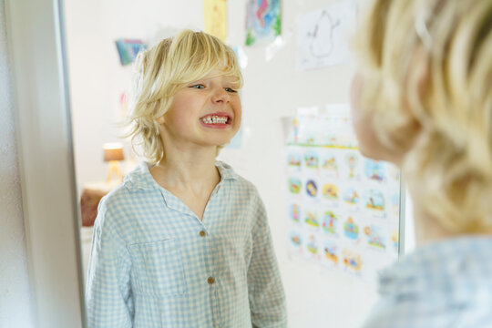 Blond boy looking at teeth in mirror at home
