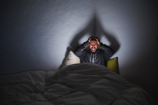 Frustrated man screaming on bed in dark room
