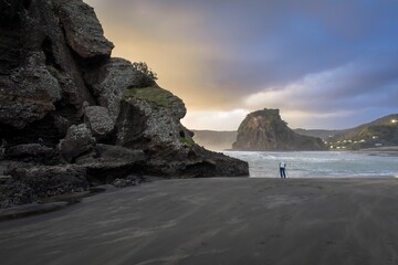 Man with a camera on a tripod taking photos on the beach. Piha, Auckland, New Zealand.
