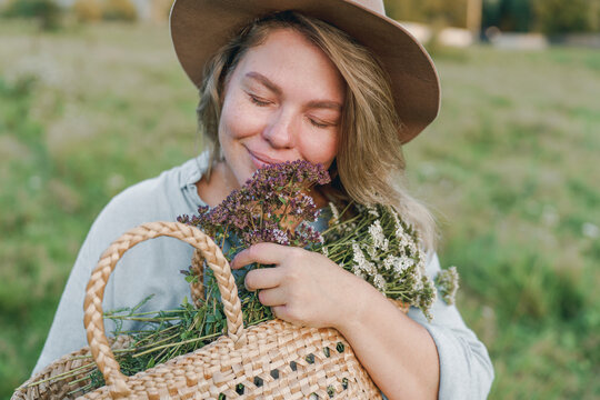 Smiling woman with eyes closed embracing basket of flowers