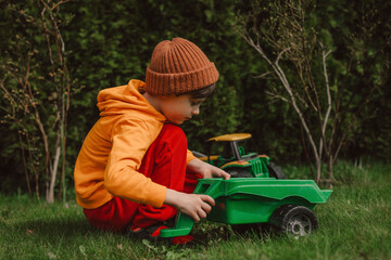 Boy crouching and playing with green toy tractor on grass in back yard
