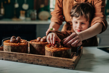 Boy and mother decorating Easter cakes with chocolate eggs in kitchen at home