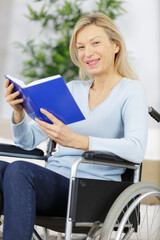 happy woman in wheelchair with a book at home - obrazy, fototapety, plakaty