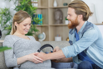 pregnant cwoman and husband holding headphones on tummy c - obrazy, fototapety, plakaty