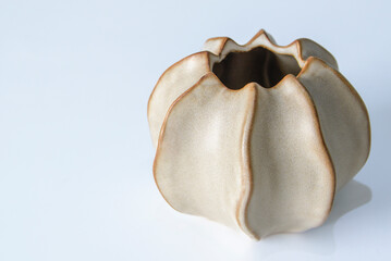 A white vase with a brown base. The vase is shaped like a flower and has a simple design