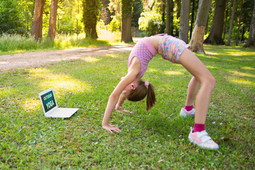 Yoga class outdoors in a summer park. A girl performs acrobatics following exercises on a computer