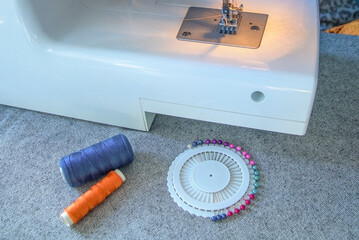 A sewing machine with a spool of thread and a pin needle on a table - obrazy, fototapety, plakaty