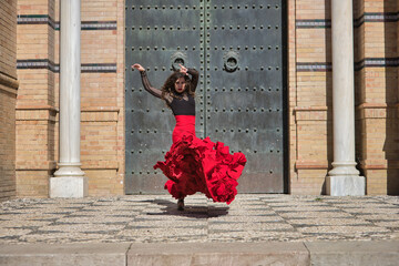 Young, beautiful, brunette woman in black shirt and red skirt, dancing flamenco in front of an old, black metal door. Flamenco concept, dance, art, typical Spanish.