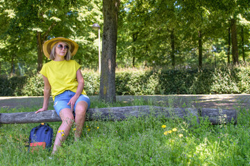 Naklejka premium Loneliness on a walk. A woman in a yellow shirt and blue shorts sits on a log in a grassy area