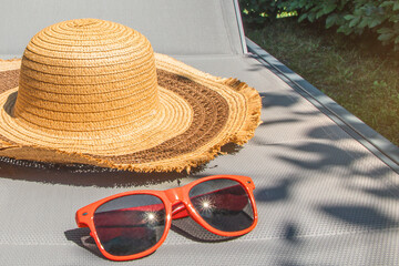 A straw hat and sunglasses are on a patio chair. Summer still life