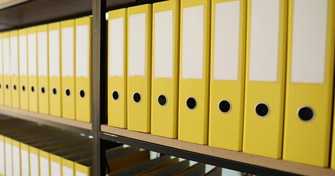 Yellow folders structure with materials on shelves of rack in company office. Room for archives and storage of documents in ring binders. Concept of saving data