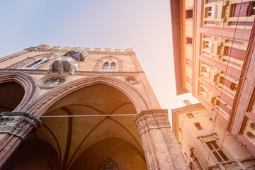 Gazing upward, this photo captures the intricate gothic arches of Palazzo della Mercanzia in Bologna, standing in harmony beside the city iconic twin towers - obrazy, fototapety, plakaty