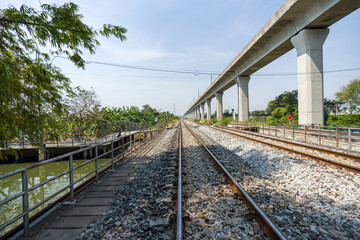 A traditional railway track lined with gravel ballast running parallel to a modern elevated rail. It showcases a juxtaposition between older and newer forms of transportation infrastructure.