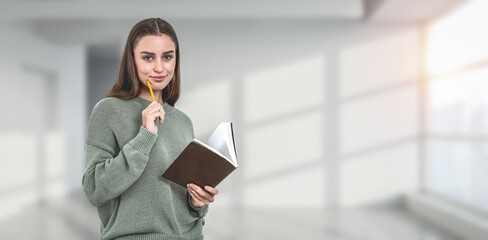 A woman holding a pencil and notebook, posing in a casual sweate