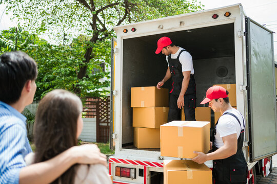 Asian and Caucasian workers in uniform unloading cardboard boxes from the truck. Delivery men unloading boxes and check the checklist with their coworkers. Professional delivery and moving service.