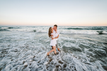 Female kisses and hugs male standing barefoot on water with big waves ocean and enjoying a summer...