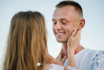 Fototapeta premium Face man closeup. Girl hands hugs boy's face and looks into his eyes and enjoy. Happy couple looking at each other walking on seashore. Man and woman stand on sand sea. Female and male on beach ocean.