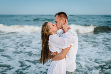 Love. Couple hugging and kissing on seashore in sea. Male kisses and hugs female standing on water with big waves ocean and enjoying a summer day. Man embraces woman walking on beach sand sea.