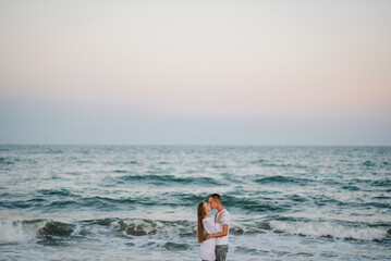 Couple in love hugging and kissing on seashore. Female kisses and hugs male standing on water with big waves ocean and enjoying a summer day. Man embraces woman walking on beach sand sea.