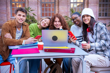 Group of smiling multiracial students with laptop sitting near campus preparing for the exam.