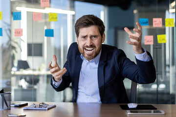 Frustrated business executive expressing anger and dissatisfaction in a modern office setting, surrounded by sticky notes and equipped with a laptop.