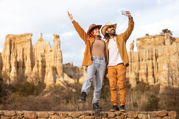 A couple is taking a picture of a mountain range. The man is holding a cell phone and the woman is...