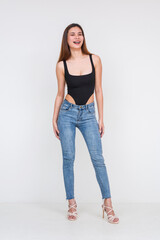 Young Asian woman in black bodysuit and jeans smiling against white background