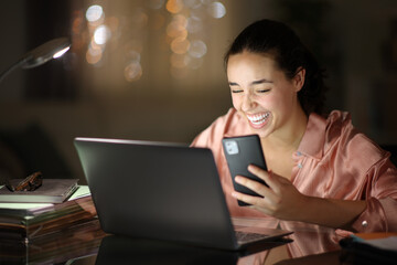 Happy tele worker in the night laughing checking phone