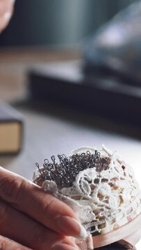 Young tailor is taking spoos from the beautiful pincushion. Many black sewing pins in a small white pillow for seamstress on the wooden table. Vertical video