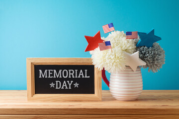 Memorial day concept with flowers decoration, chalkboard and USA flags on wooden table over blue...