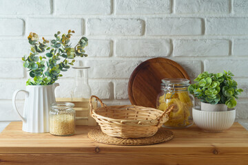 Empty basket on kitchen table with food jars and plants over white brick wall  background.  Kitchen...