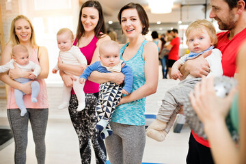 Group exercise class, mother working out with baby in gym. Moms staying active while boding with...