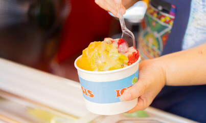 Closeup of woman's hands holding cup with homemade fruity sorbet ice cream served in a plastic...