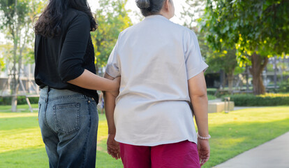Rear view shot of young woman with old grandmother walking in the park.