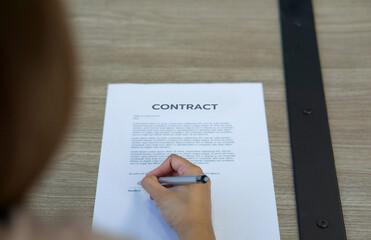 Closeup woman hand signing her name on a contract document on wooden table.