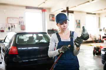 Female auto mechanic repairing, maintaining car. Beautiful woman working in a garage, wearing blue...