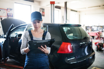 Female auto mechanic using diagnostic tool, scanner, running diagnostic on car. Beautiful woman...
