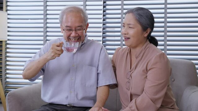Asian grandfather drinking tea and talking with grandmother in the living room. Senior couple enjoy chatting together at home