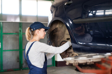 Female auto mechanic elevating car on car lift, checking breaks. Beautiful woman working in a...