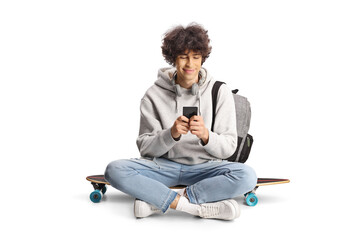 Male student with a backpack sitting on a skateboard and using a smartphone
