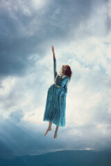 Elegant tender young girl in dress levitating against cloudy sky background. Reaching endless...