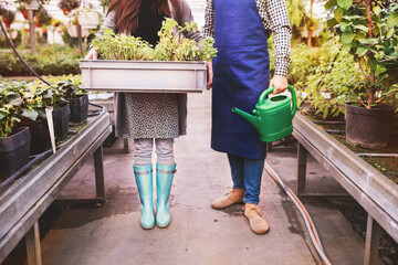 Close up on legs of gardener and customer holding watering can and plastic crate, plant tray. Small...