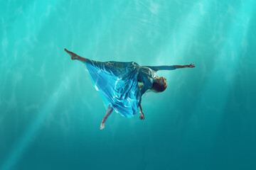 Lost in the current. Young redhead woman in elegant, tender white dress drowning into cyan water, deep ocean with sunlight. Concept of surrealism, beauty, mystery and fantasy, freedom